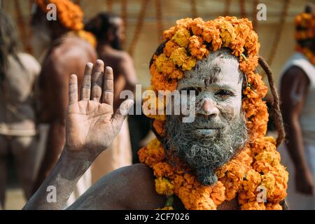 Allahabad City, Inde - FÉVRIER, 2018: Hindu sadhu avec le visage peint avec des fleurs de frêne et de safran autour de la tête et du cou debout sur la rue et en agitant la main à la caméra pendant le festival Prayag Kumbh Mela Banque D'Images