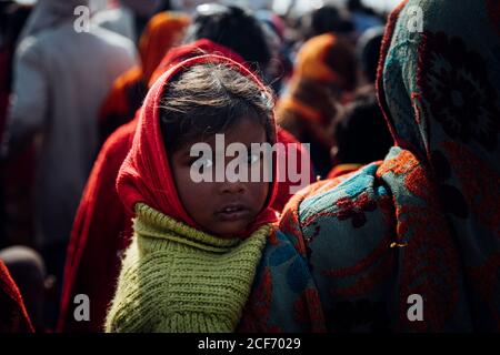 Allahabad City, Inde - FÉVRIER, 2018: Petite fille en foulard rouge et pull vert assis dans les bras de la récolte femme marchant dans la rue dans la foule de pèlerins pendant le festival Prayag Kumbh Mela Banque D'Images