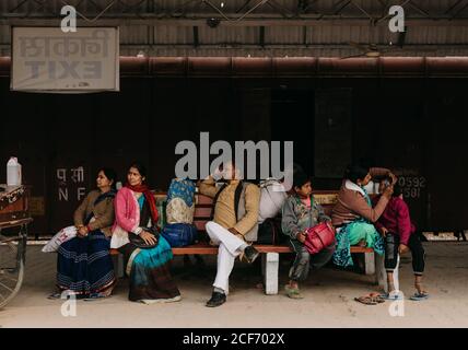 Prayag Kumbh Mela Festival, Allahabad, Inde - février, 2018:femmes en vêtements rouges et bleus homme et enfants festifs attendant le transport assis sur le banc de gare et regardant loin Banque D'Images