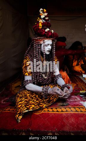 Allahabad City, Inde - FÉVRIER, 2018: Hindou sadhu Saint homme avec visage peint portant un costume traditionnel coloré assis sur le tapis pendant le festival Prayag Kumgh Mela Banque D'Images