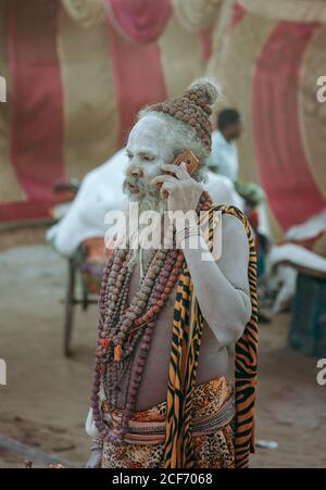 Allahabad City, Inde - FÉVRIER, 2018: Hindou sadhu avec le visage peint avec debout sur la rue parlant au téléphone pendant le festival Prayag Kumgh Mela Banque D'Images