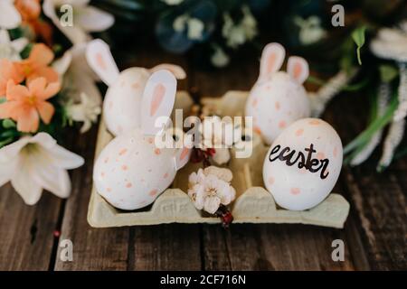 Oeufs de Pâques avec oreilles de lapin peintes par les enfants dans un coquetier avec fleurs Banque D'Images