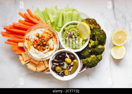 De dessus appétissant sauce verte de houmous saine couper les concombres de carotte et brocoli vert concombres salés décorés de tranches de citron bols blancs sur la table Banque D'Images