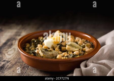 Ragoût de pois chiches avec des épinards et du poisson de morue ou vigile potaje sur une table en bois Banque D'Images