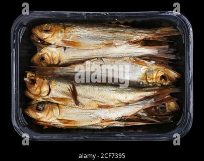 Sprat fumé chaud poisson de mer Baltique avec têtes et guts dans une boîte en plastique . Isolé sur macro studio noir Banque D'Images