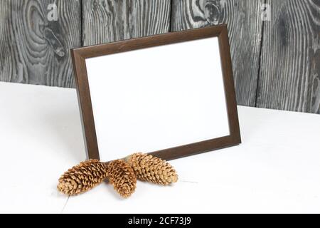 Cadre photo en bois avec un champ blanc pour une inscription ou une photo. À proximité sont des cônes de sapin. Banque D'Images