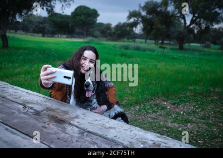 Par-dessus une jeune femme heureuse souriant pendant un câlin noir et blanc tout en filant selfie sur téléphone mobile dans le parc Banque D'Images