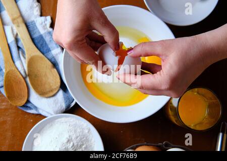 Femme méconnaissable cassant l'œuf de poulet cru sur un bol avec du sucre près de la farine de blé pendant la préparation de la pâtisserie à la maison Banque D'Images