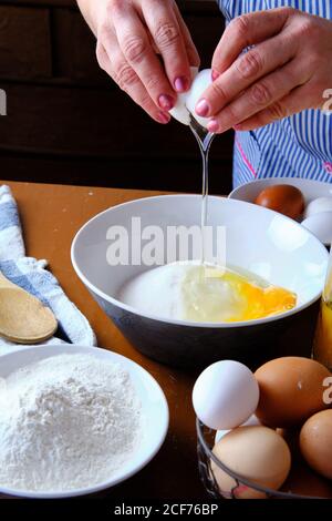 Femme méconnaissable cassant l'œuf de poulet cru sur un bol avec du sucre près de la farine de blé pendant la préparation de la pâtisserie à la maison Banque D'Images