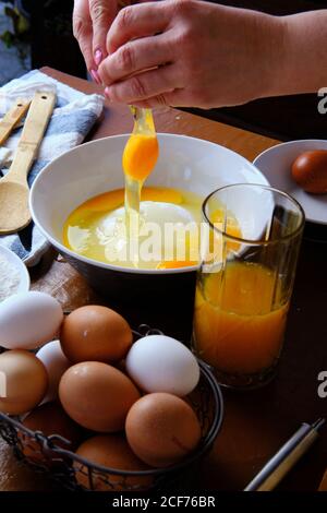 Femme méconnaissable cassant l'œuf de poulet cru sur un bol avec du sucre près de la farine de blé pendant la préparation de la pâtisserie à la maison Banque D'Images