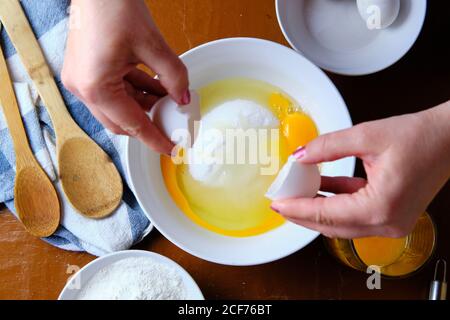 Femme méconnaissable cassant l'œuf de poulet cru sur un bol avec du sucre près de la farine de blé pendant la préparation de la pâtisserie à la maison Banque D'Images