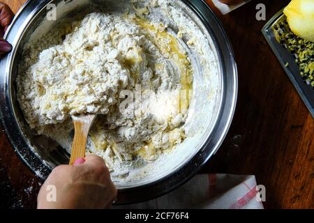 De la personne anonyme ci-dessus en utilisant une cuillère en bois pour mélanger doux pâte à pâtisserie dans un bol en métal sur une table dans la cuisine Banque D'Images