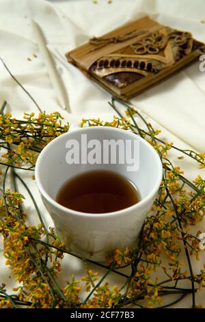 Tasse blanche avec thé placée sur le lit avec des fleurs jaunes et bouquet pour un délicieux petit déjeuner au lit Banque D'Images