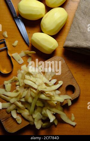 Vue de dessus des pommes de terre pelées et des pelures de pommes de terre sur la coupe planche avec couteau dans la cuisine moderne Banque D'Images