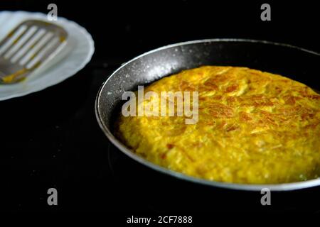 De dessus la poêle en métal avec savoureuse omelette dorée espagnole avec huile d'olive dans la cuisine Banque D'Images