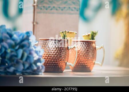 Cocktail froid de Mule de Moscou avec bière au gingembre et vodka avec citron vert servi dans des mugs traditionnels en cuivre sur le comptoir avec fleurs Banque D'Images