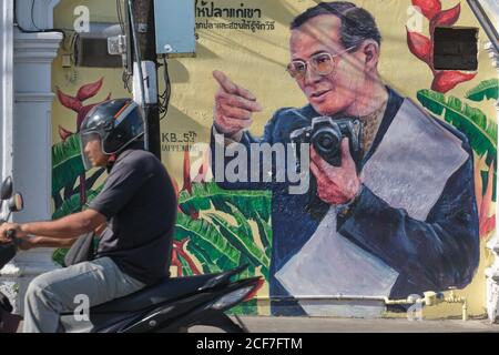 Un chauffeur de moto passe devant un portrait du roi thaïlandais Bhumipol Adulyadej, peint sur les murs de la vieille ville de Phuket, en Thaïlande Banque D'Images