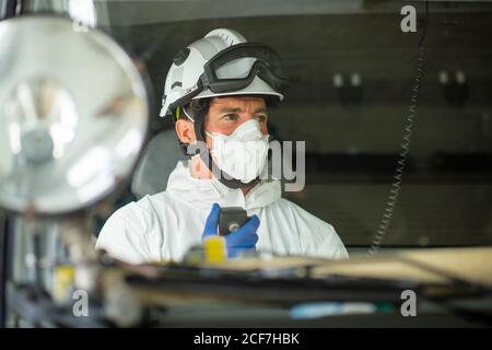 Pompier portant un respirateur et un casque assis dans une voiture d'incendie et utilisation du talkie-walkie Banque D'Images