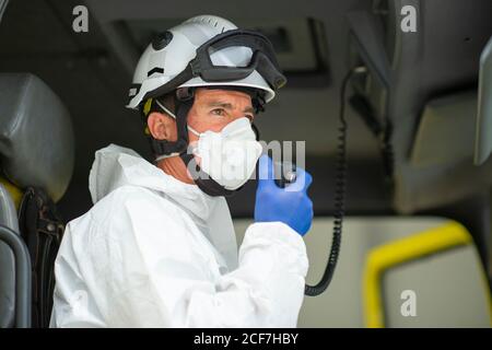 Vue latérale pompier portant un respirateur et un casque assis dans le feu voiture et talkie-walkie Banque D'Images