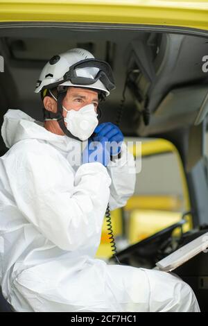 Vue latérale un pompier sérieux portant un respirateur et un casque assis voiture de pompiers Banque D'Images