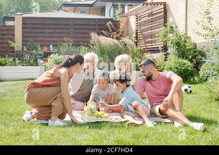 Grande famille de plusieurs générations ayant pique-nique sur la pelouse dans l'arrière-cour chaude journée d'été Banque D'Images