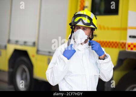 Pompier sérieux en costume de protection et portant un respirateur sur le feu au cours de la pandémie du coronavirus Banque D'Images