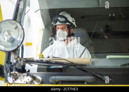 Pompier sérieux portant un respirateur et un casque assis dans une voiture d'incendie Banque D'Images