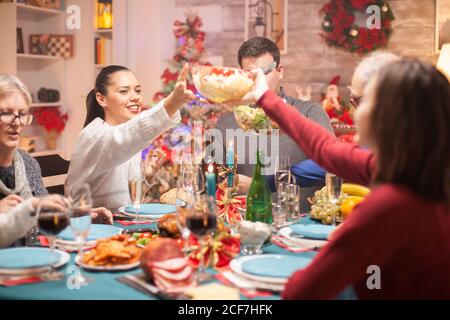 Bonne femme qui passe la salade sur la table à sa fille lors du dîner de noël en famille. Banque D'Images