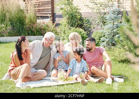 Portrait de famille joyeuse de plusieurs générations assis sur la pelouse dans l'arrière-cour le jour d'été ensoleillé, pique-nique Banque D'Images