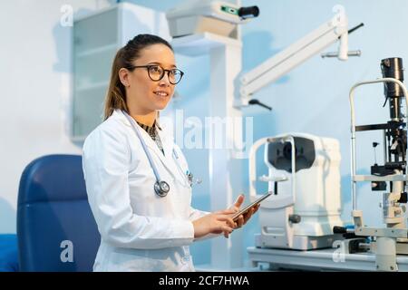 Jeune femme gaie médecin en uniforme en utilisant un téléphone dedans pause dans la chambre Banque D'Images