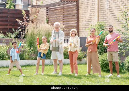 Les grands membres de la famille qui se tiennent sur une pelouse verte ont du plaisir à poser sur caméra avec pistolets à eau Banque D'Images