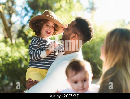 Joyeux jeune famille multiraciale avec de petits enfants qui s'amusent ensemble tout en se reposant dans un parc verdoyant par une belle journée d'été Banque D'Images