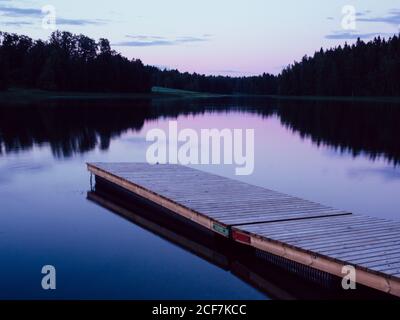 Paysage finlandais avec plancher en bois dans l'eau calme du lac contre la forêt sombre le soir Banque D'Images