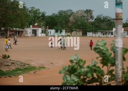 Gambie, Afrique - 5 août 2019: Des garçons pauvres noirs jouant au football avec plaisir sur le terrain dans un quartier spacieux en journée Banque D'Images