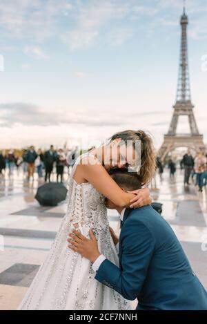 Tenue élégante bleue sur le genou et Embrasser une mariée satisfaite en robe de mariage blanche avec la Tour Eiffel en arrière-plan Banque D'Images