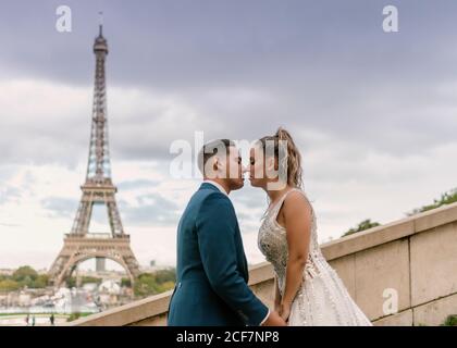 Marié en costume bleu et mariée en robe de mariée blanche Embrasser passionnément la Tour Eiffel en arrière-plan à Paris Banque D'Images