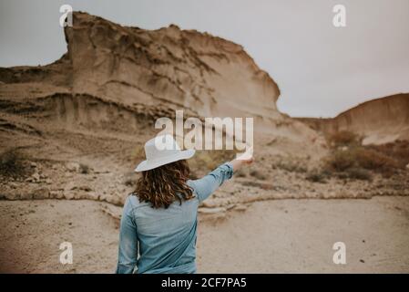 Vue arrière d'une femme méconnaissable vêtue de vêtements décontractés sur les dunes de sable du désert et montrant le jour sombre Banque D'Images