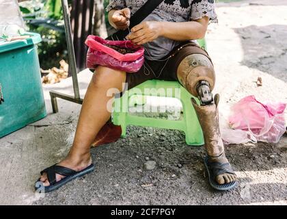 De dessus de la récolte anonyme homme handicapé en tenue décontractée avec une prothèse de jambe assise sur une chaise et en train de trier les baies rue Banque D'Images