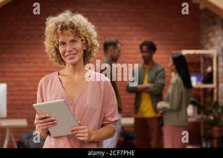 Portrait d'une femme de premier plan avec une tablette numérique souriante caméra avec son équipe en arrière-plan au bureau Banque D'Images
