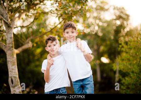 Les deux frères souriants sont vêtus de t-shirts blancs et de jeans et regarder la caméra tout en se tenant dans le parc vert jour d'été Banque D'Images