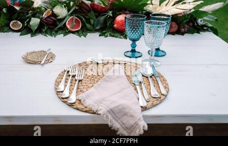 Table en bois blanc sans tissu décorée de fruits et de fleurs disposition et servi avec des couverts et serviettes de linge en osier serviettes et verres bleus Banque D'Images