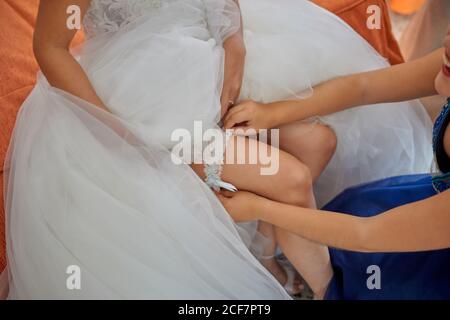 De dessus de la petite demoiselle d'honneur aidant la mariée à porter le mariage enfiler la jarretière sur la jambe pendant la préparation le matin Banque D'Images