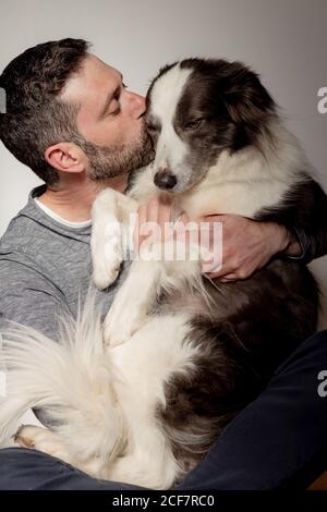 Homme en tenue décontractée donnant un câlin et baiser à un chien bien-aimé Border Collie à la maison Banque D'Images