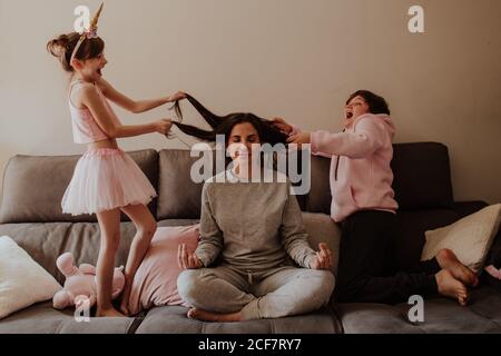 Une petite fille excitée et un garçon de l'adolescence tirant les cheveux de la femme adulte assise dans Lotus poser sur le lit et méditer Banque D'Images