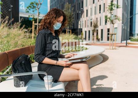 Femme d'affaires travaillant sur un banc de parc à l'aide de sa tablette numérique pendant la pandémie du virus corona. Banque D'Images