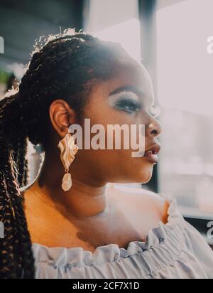 Portrait de côté de la jeune femme noire, avec une belle courbure et rétro-éclairée, avec un maquillage brillant dans une robe de hors-épaule Banque D'Images
