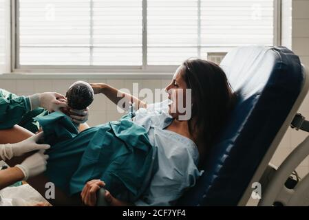 Une femme tentait de saisir la poignée et de brander la douleur tout en donnant naissance à bébé sur une chaise médicale dans un hôpital moderne Banque D'Images