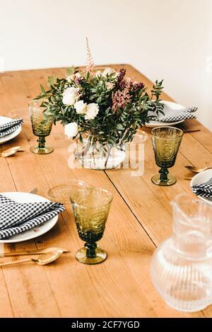 Bouquet de fleurs diverses et brindilles de plantes vertes dans un vase avec de l'eau sur une table en bois pour un repas Banque D'Images