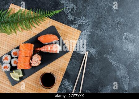 Sashimi roule sur une pierre noire slatter. Gros plan de l'ensemble de sushis avec des baguettes et du soja Banque D'Images