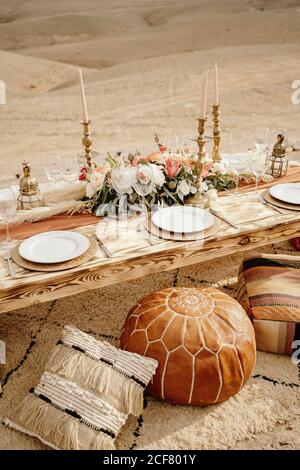 Depuis le dessus de la longue table en bois décorée de fleurs et bougies et servi avec des assiettes blanches placées sur la moquette près Sièges arabes traditionnels avec dunes de sable en arrière-plan Banque D'Images